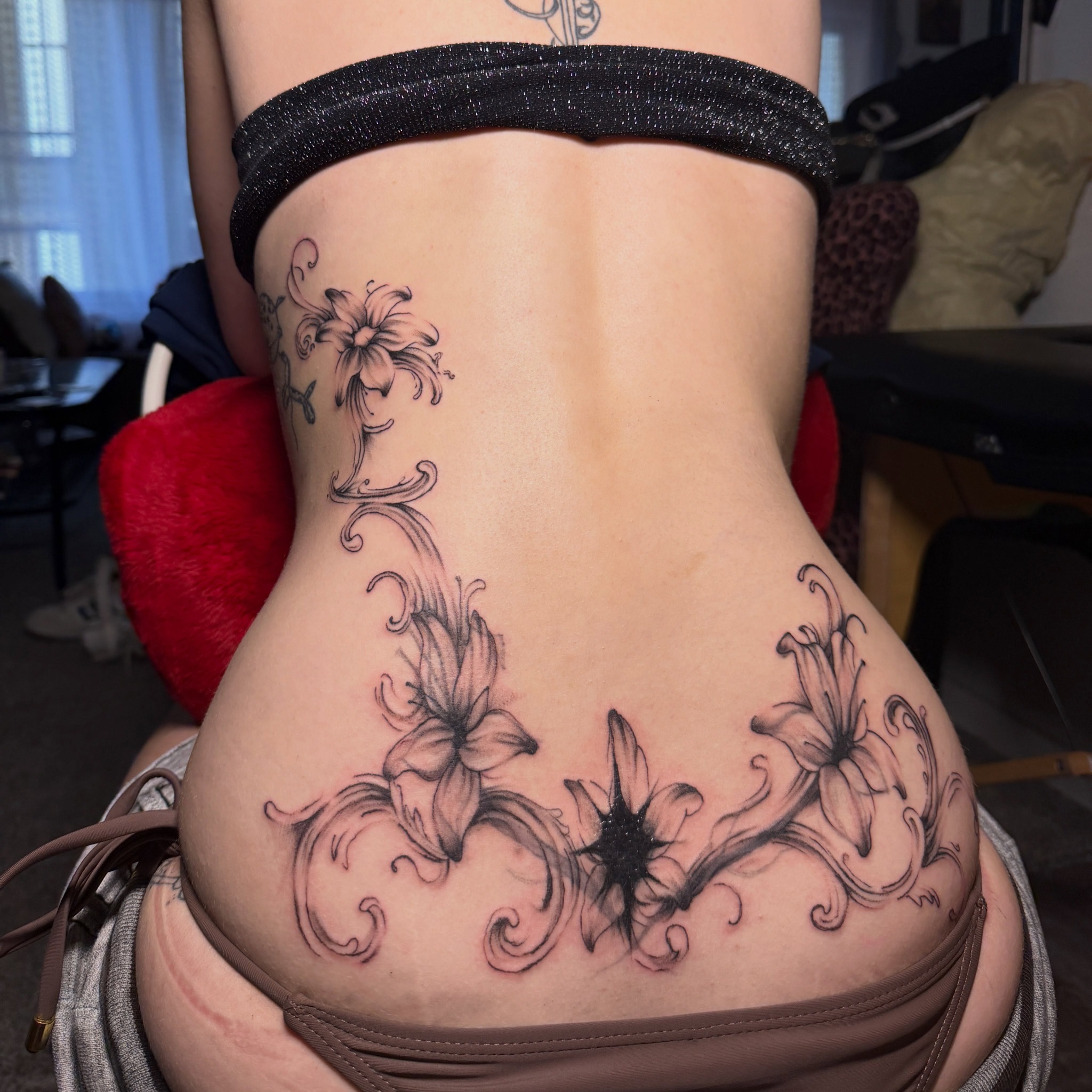 Fine-line botanical ornament tattoo across a client's lower back