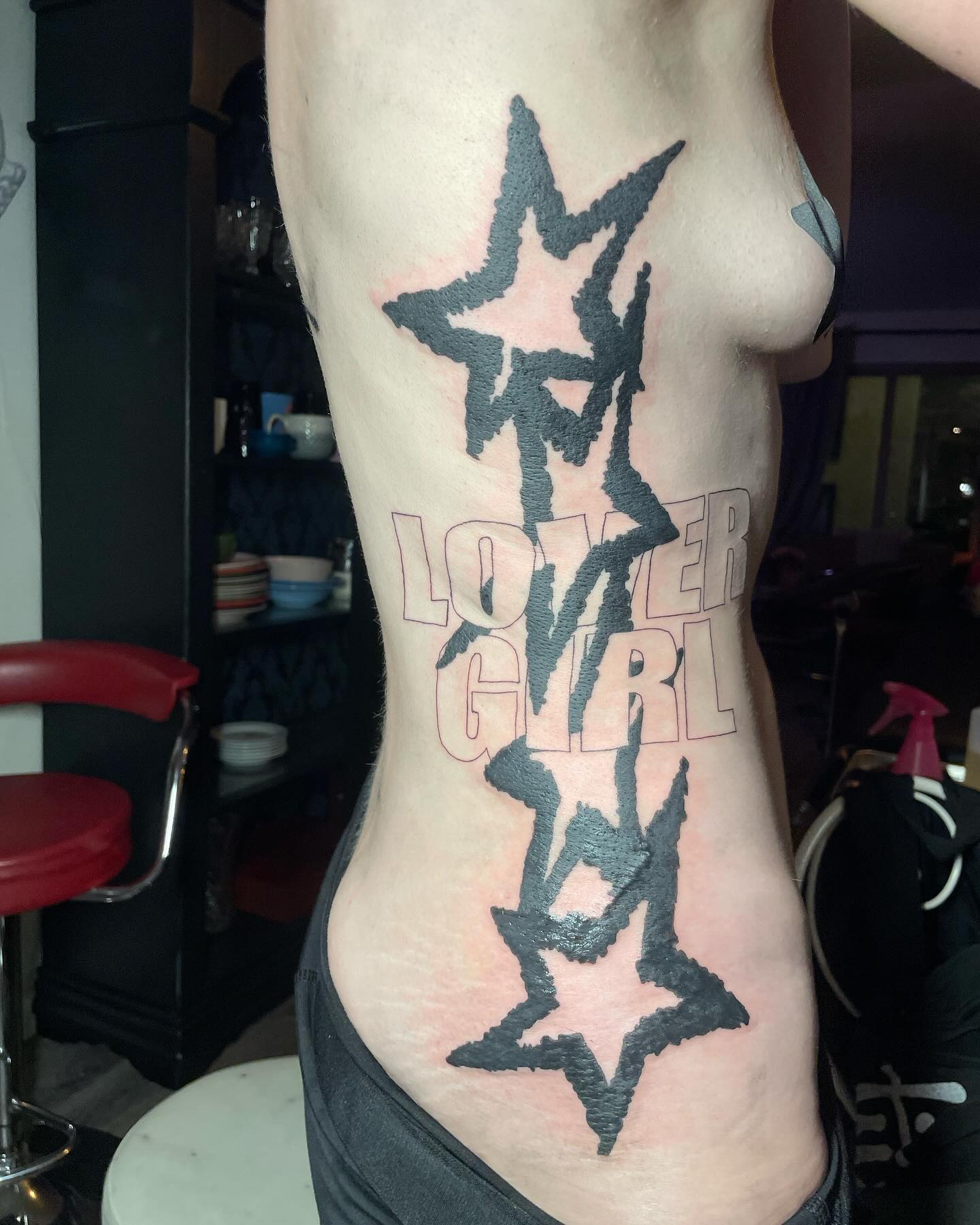 Black and red star tattoos with outlined lettering along a client's side